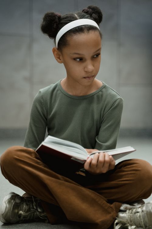 Free A young girl with a book, concentrating on her studies indoors, evoking curiosity. Stock Photo