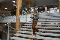 Woman in Gray Long Sleeve Shirt and Brown Pants Standing on Gray Staircase