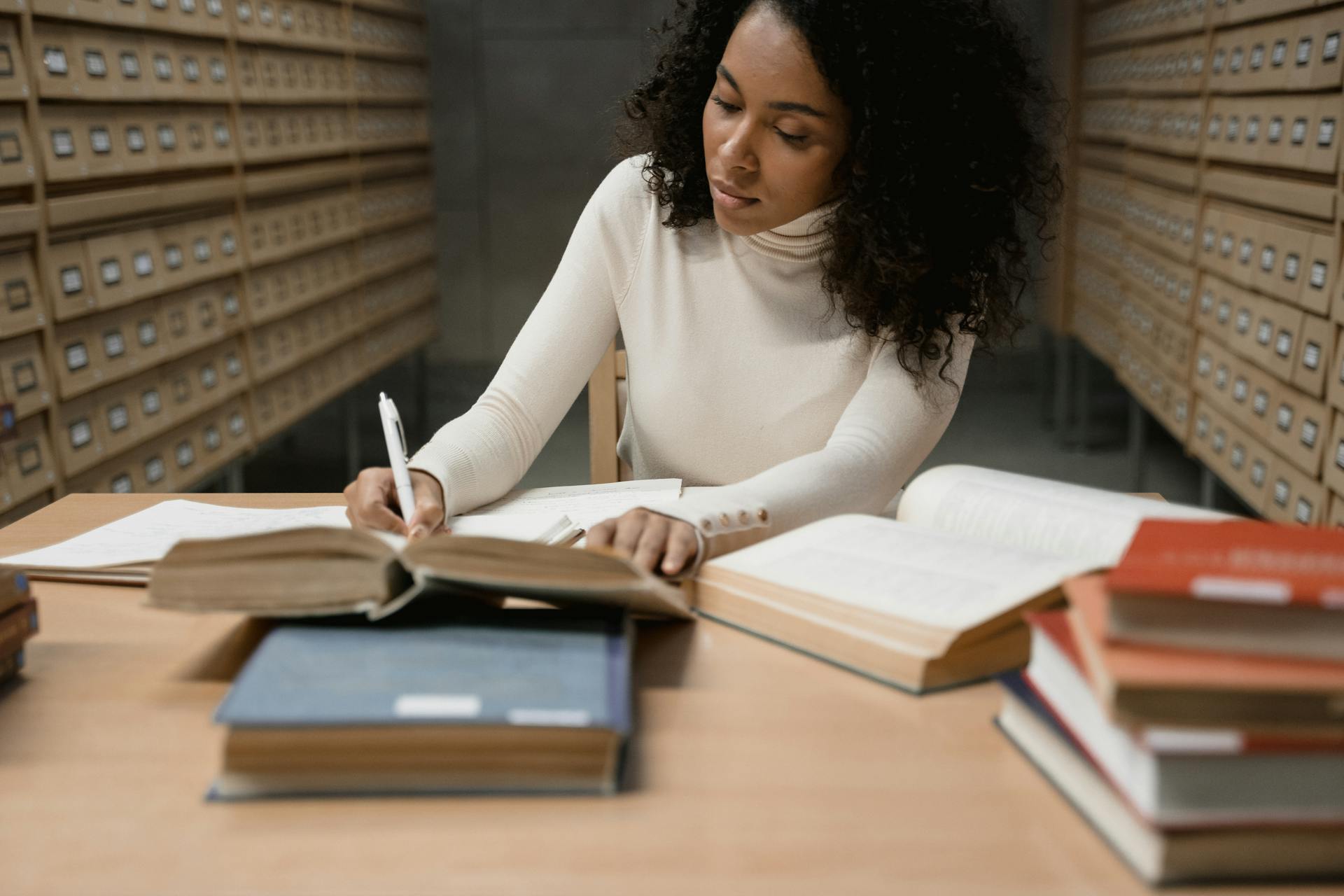 Young woman engaged in research and writing in a library setting.