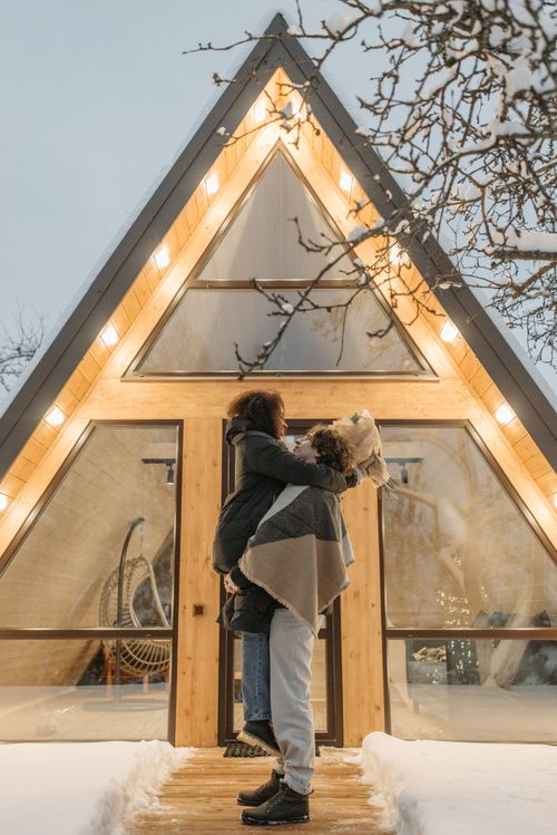 Free Loving couple embracing in front of a cozy A-frame cabin during winter. Stock Photo