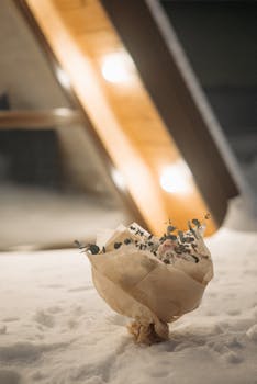 A beautifully wrapped flower bouquet resting on snow against a warmly lit modern building during winter.