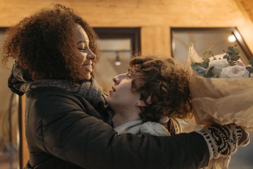 Free Loving couple in winter clothing sharing a warm embrace indoors with a bouquet of flowers. Stock Photo