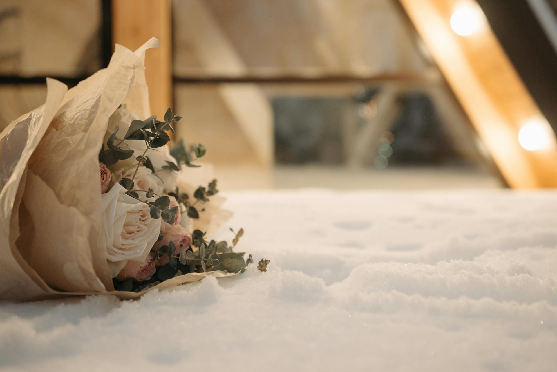 Elegant bouquet of roses wrapped in parchment paper rests on a snowy surface, evoking a winter romance.