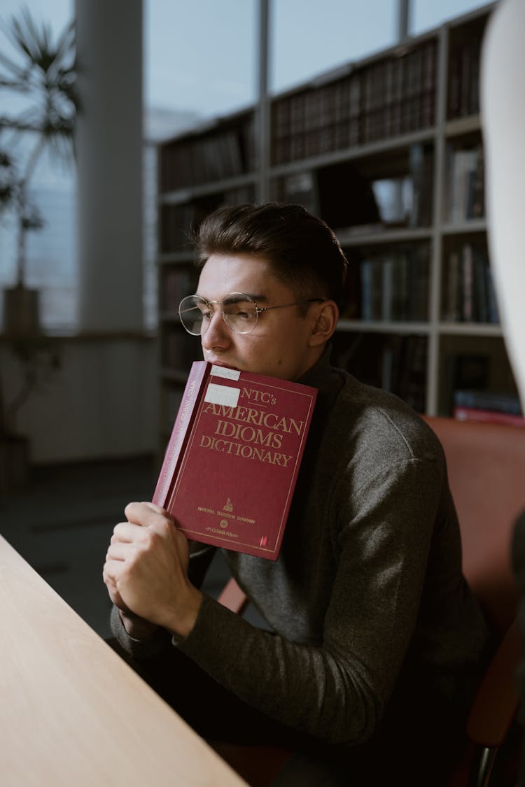 A Man In A Sweater Holding A Dictionary