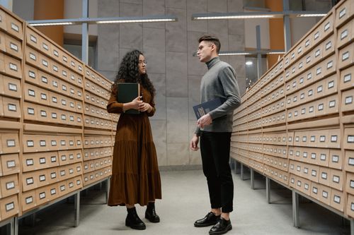 Free A man and woman standing in a library aisle discussing academic materials. Stock Photo