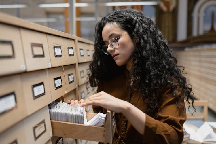 A Woman Wearing Eyeglasses Browsing Records In A Drawer 