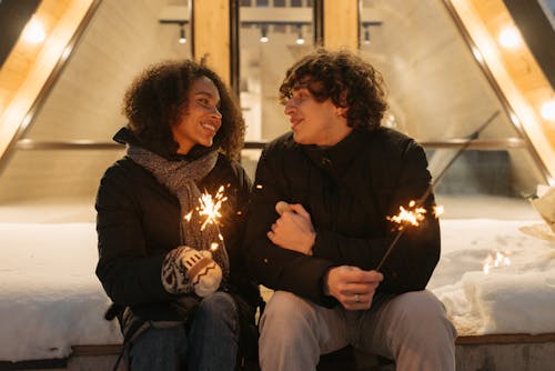 A couple enjoying a romantic winter evening outdoors, sharing flashlers and smiles.