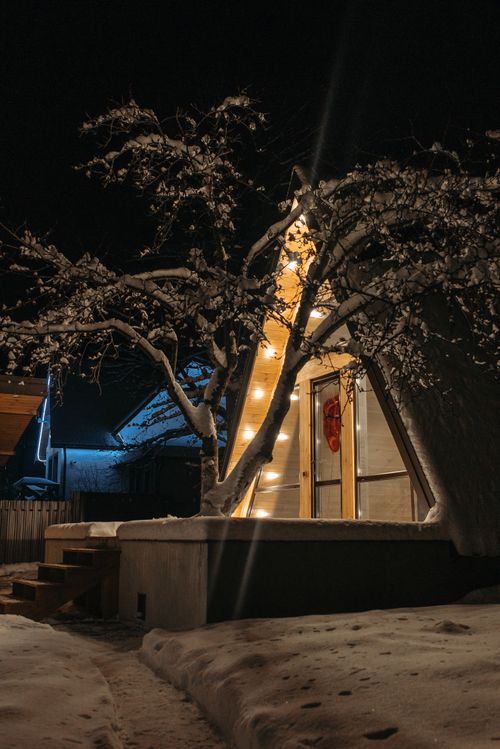 Free A snowy A-frame cabin illuminated with warm lights, capturing a tranquil winter night scene. Stock Photo