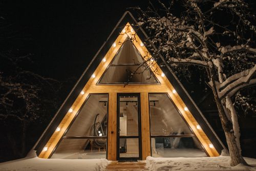 Free A beautifully lit triangular wooden house surrounded by snow at night. Stock Photo