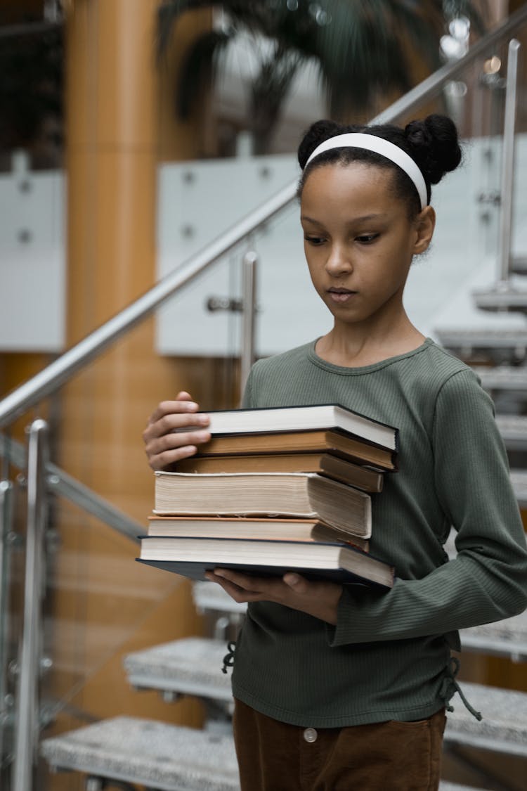 A Girl Carrying A Pile Of Books