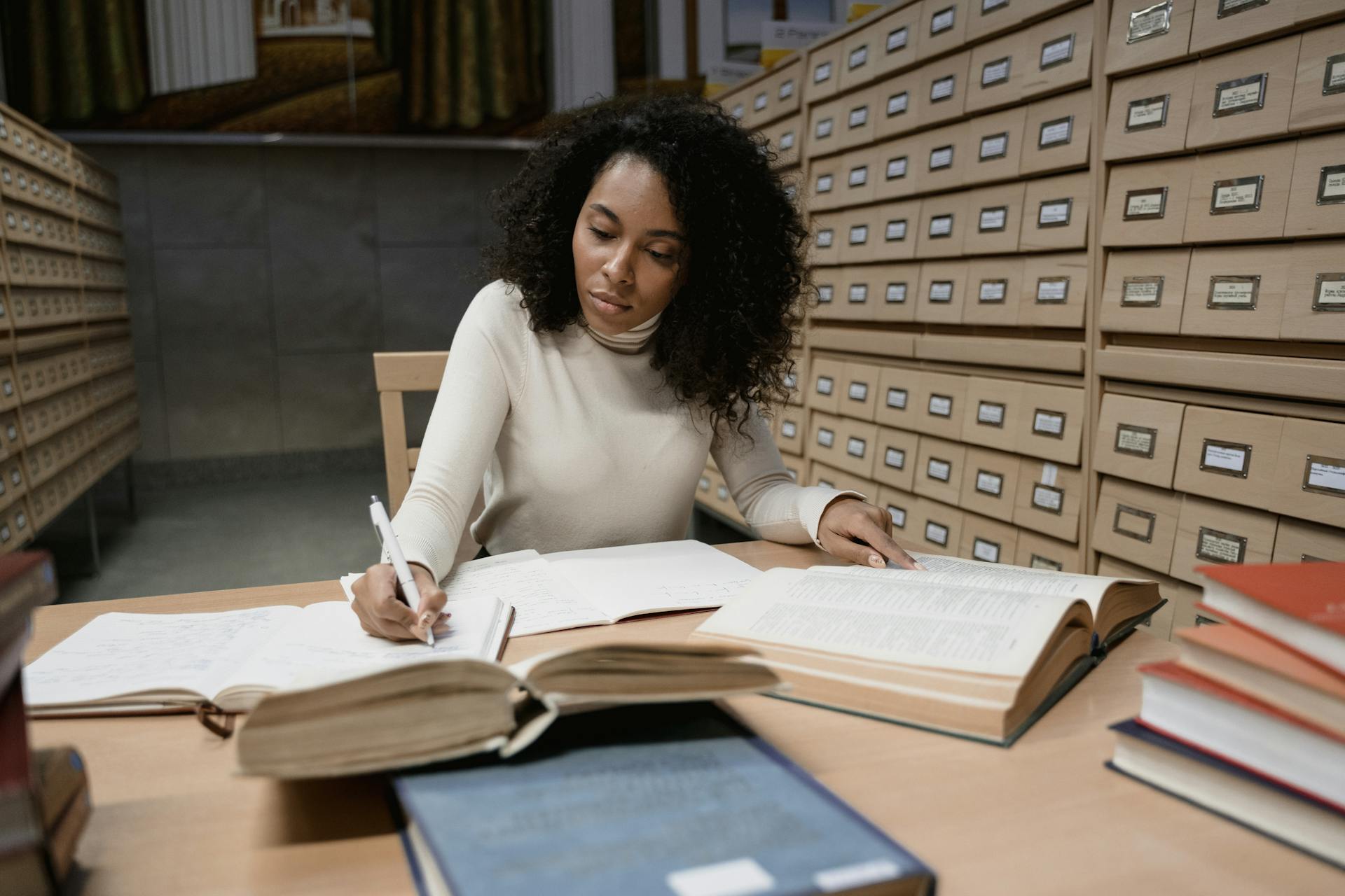 Woman taking notes in a library with books and a card catalog for research purposes.