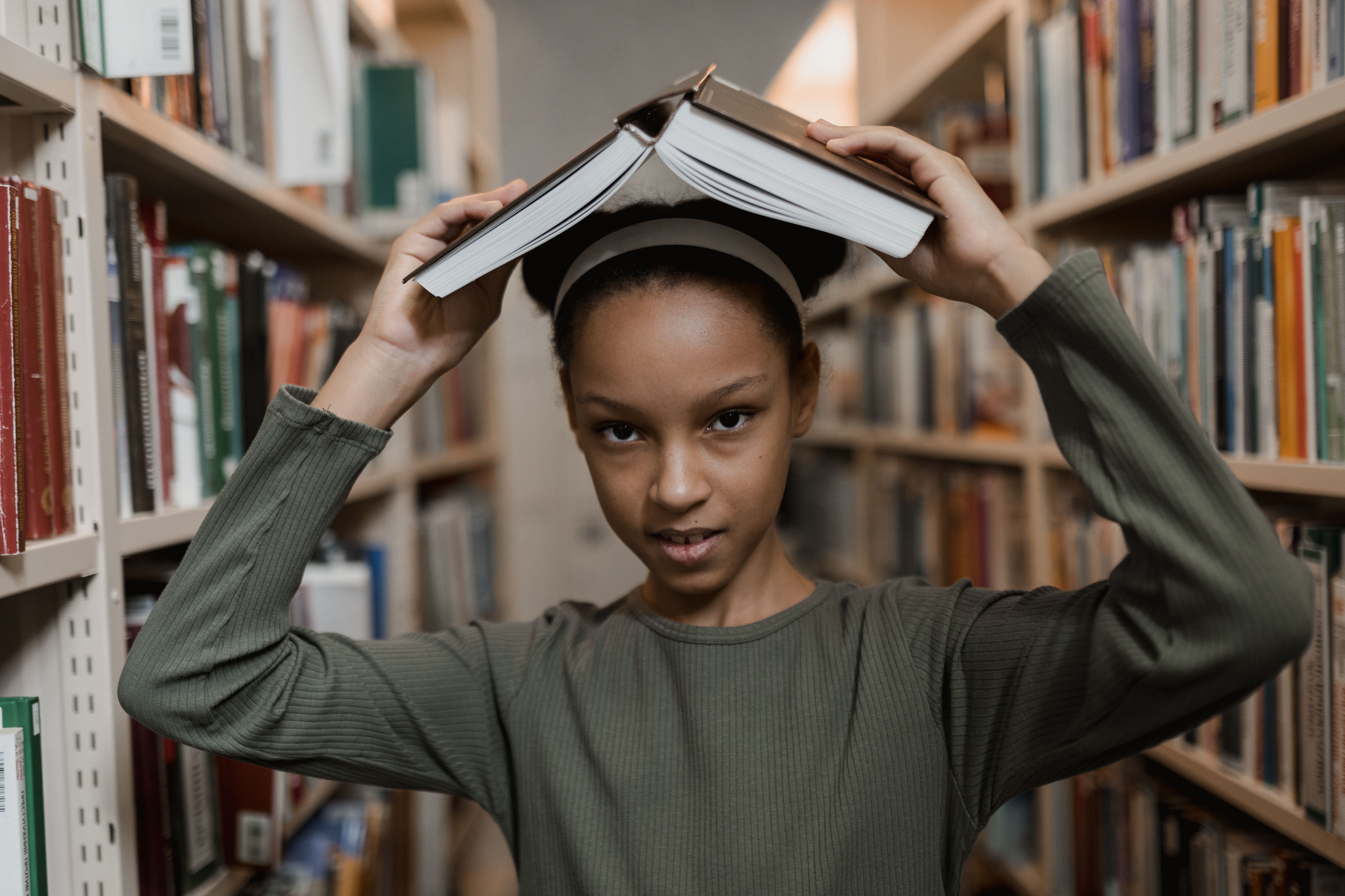 Girl in Green Long Sleeves Holding a Book Above Her Head · Free Stock Photo