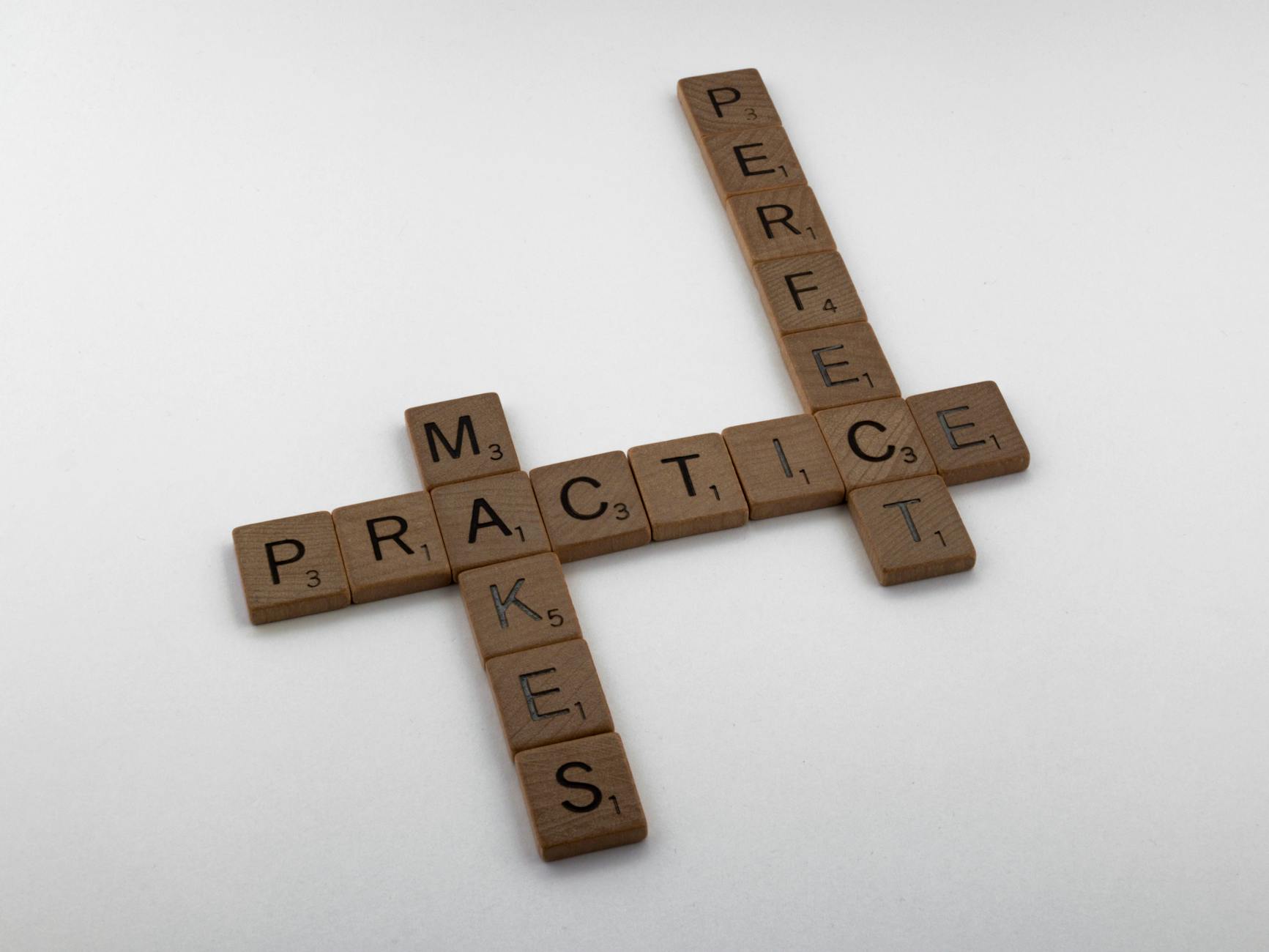 3rd grade spelling words practice Wooden Scrabble tiles forming the phrase 'Practice Makes Perfect' on a white surface. Scrabble is an excellent game for 3rd grade spelling words practice.