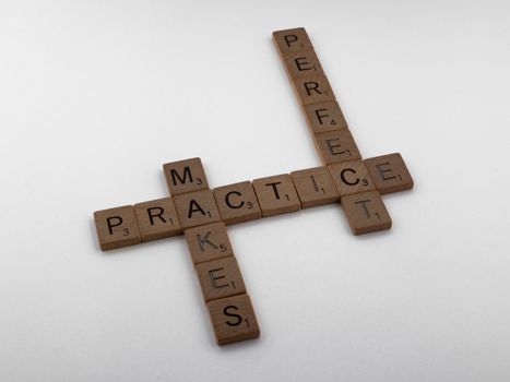 Wooden Scrabble tiles forming the phrase 'Practice Makes Perfect' on a white surface.