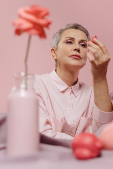 Senior woman in pink attire admiring delicate pink roses in a serene setting.