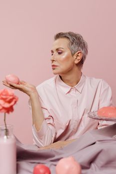 Stylish woman in pastel setting holding pink fruit, showcasing beauty and elegance.