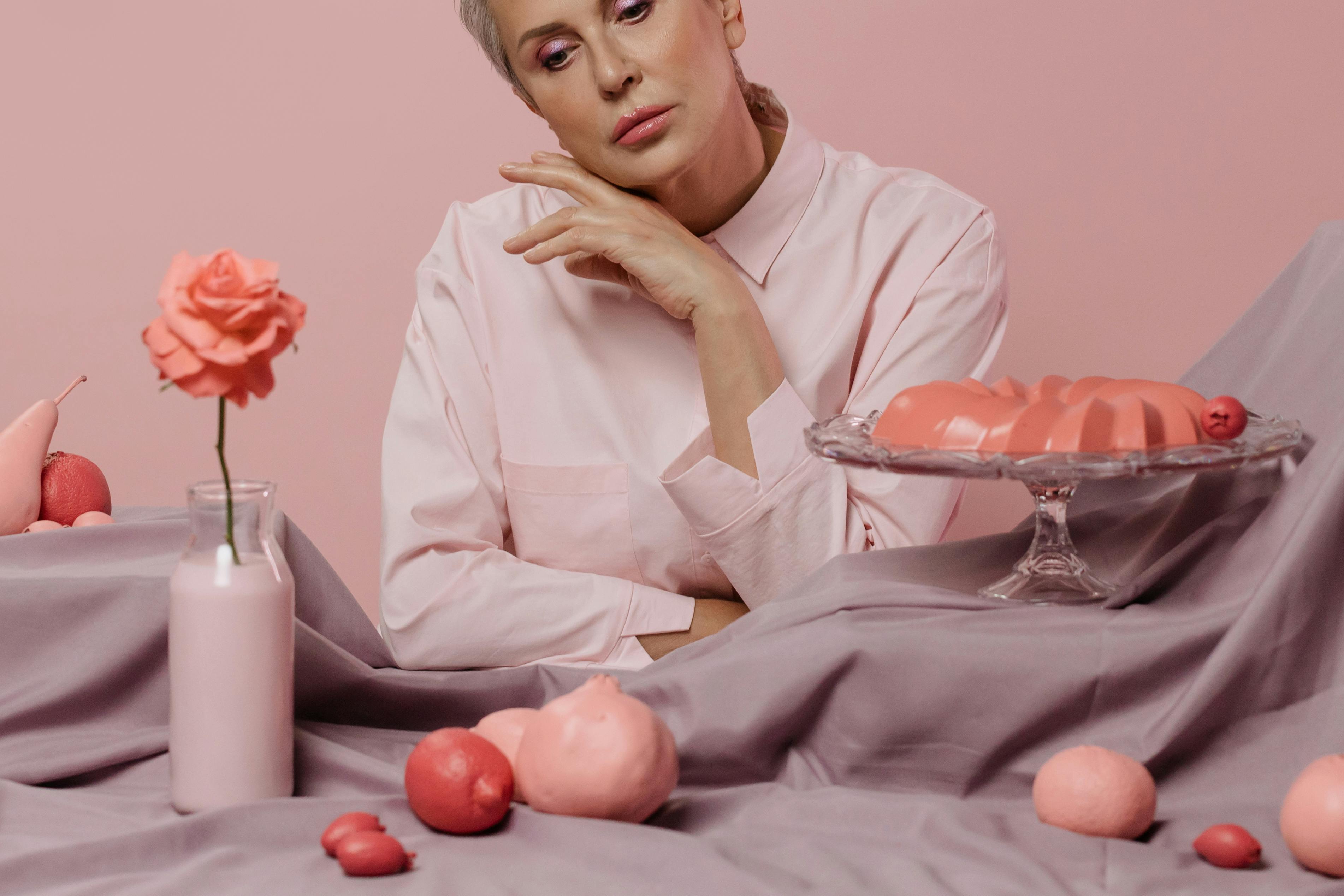 穿着淡粉色服装的女人在柔和的背景上优雅地摆出粉红色主题的装饰和甜点