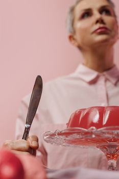 Woman with knife and jelly on pink background, capturing elegance and culinary art.