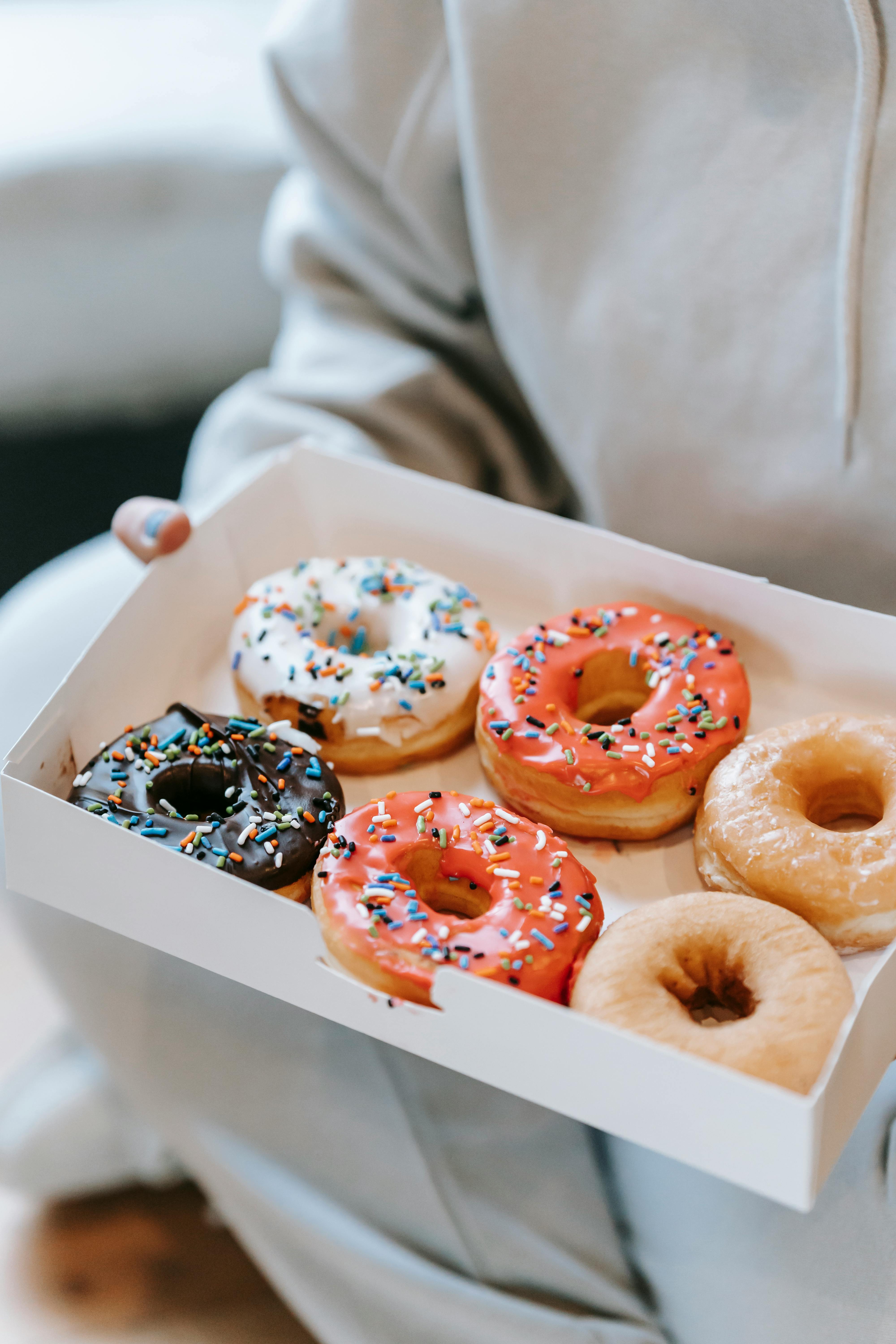 crop unrecognizable person demonstrating box with delicious doughnuts