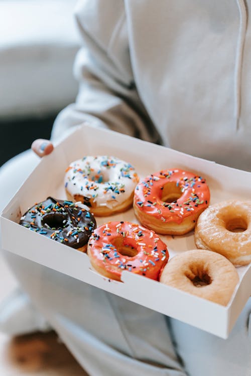 Crop unrecognizable person demonstrating box with delicious doughnuts