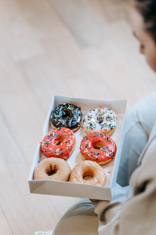 High angle crop faceless person demonstrating tasty sweet doughnuts in carton box in light room