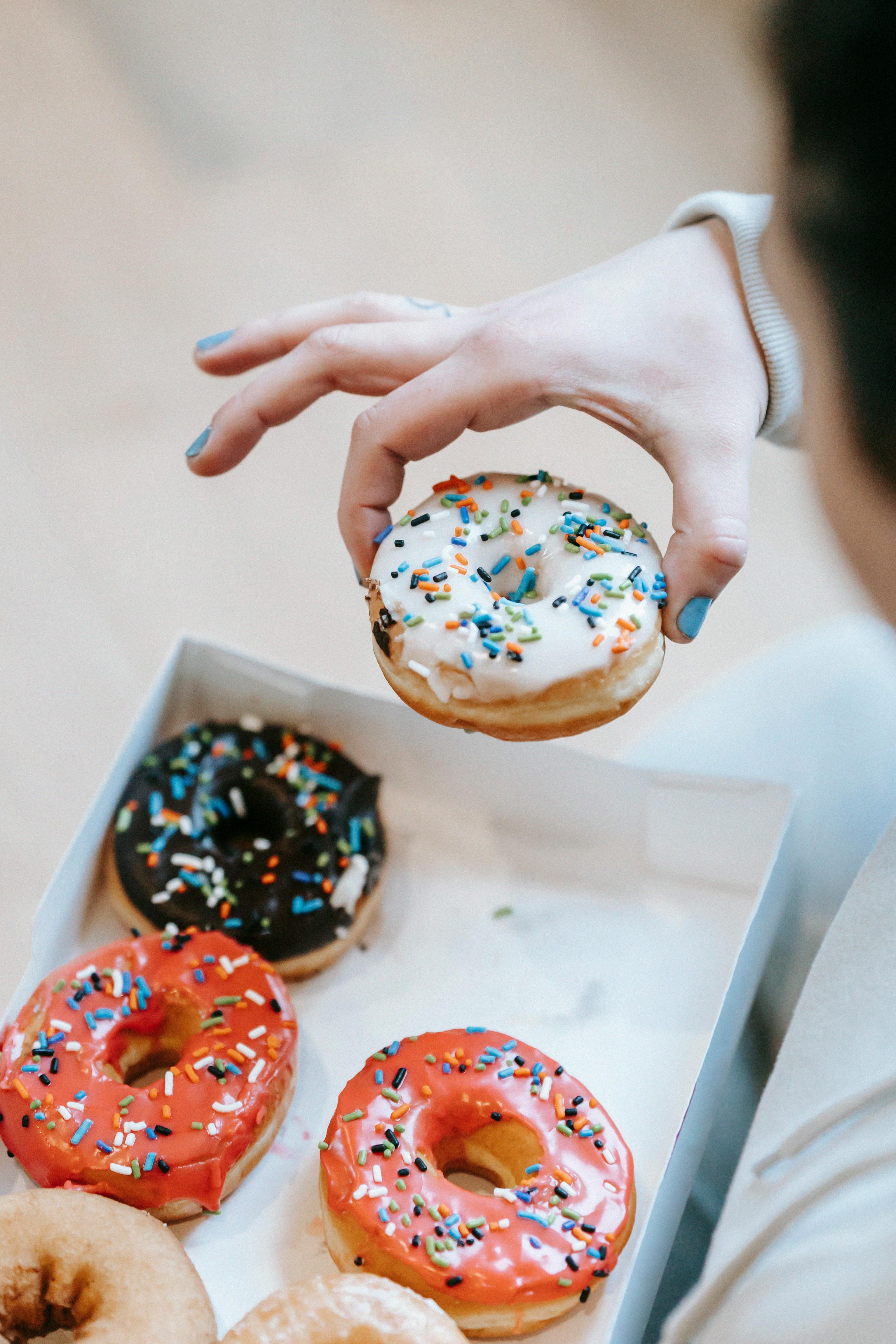 crop faceless woman picking yummy doughnut from box