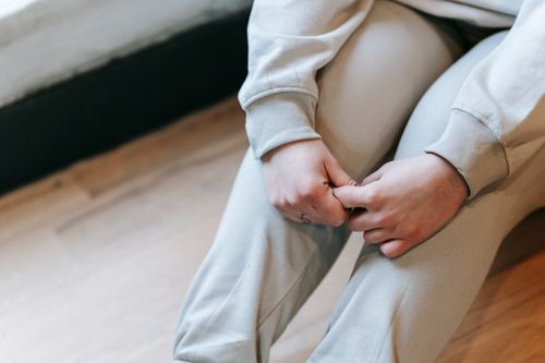 Free From above crop anonymous plus sized female in comfy clothes sitting on floor with hands on legs in light room Stock Photo
