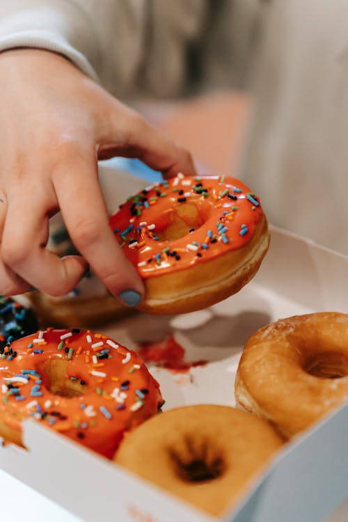 Crop anonymous female taking delicious donut covered with multicolored sweet sprinkles from carton box