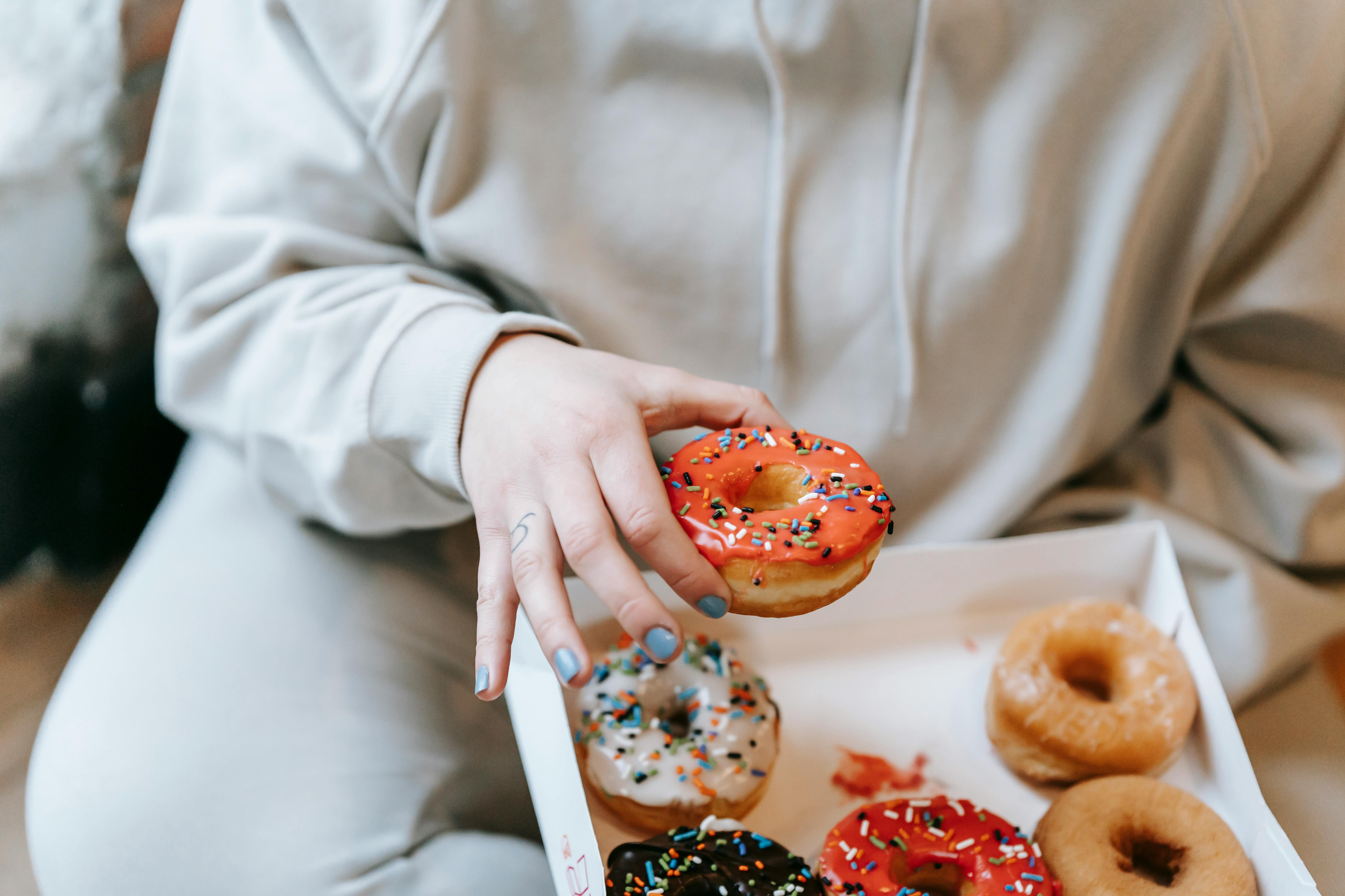 crop faceless woman taking appetizing donut from box