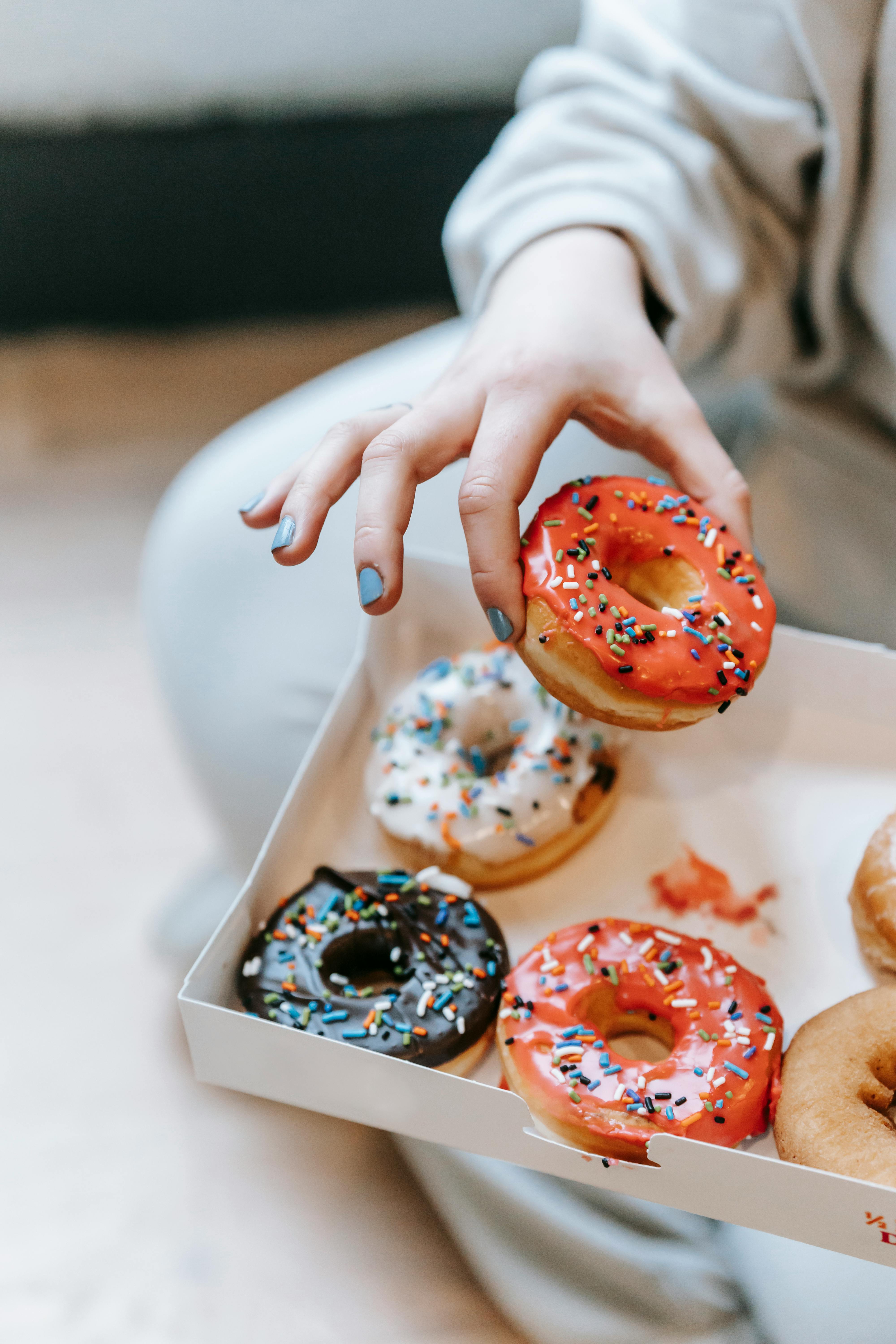 crop faceless woman taking sweet donut from box