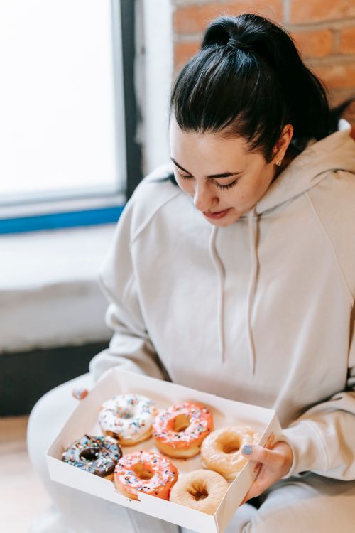 Free Young plump female in casual clothes taking box with assorted yummy fresh donuts in light room Stock Photo
