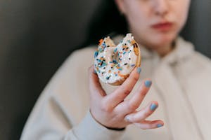 Crop blurred female wearing comfy loose clothes chewing and showing bitten tasty doughnut