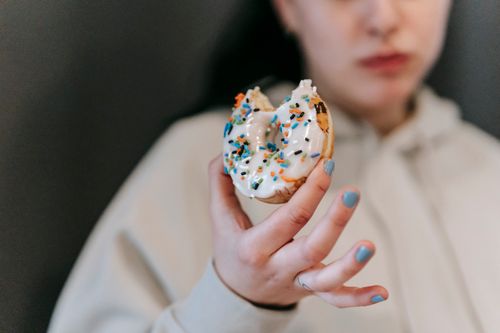 Free Crop blurred female wearing comfy loose clothes chewing and showing bitten tasty doughnut Stock Photo