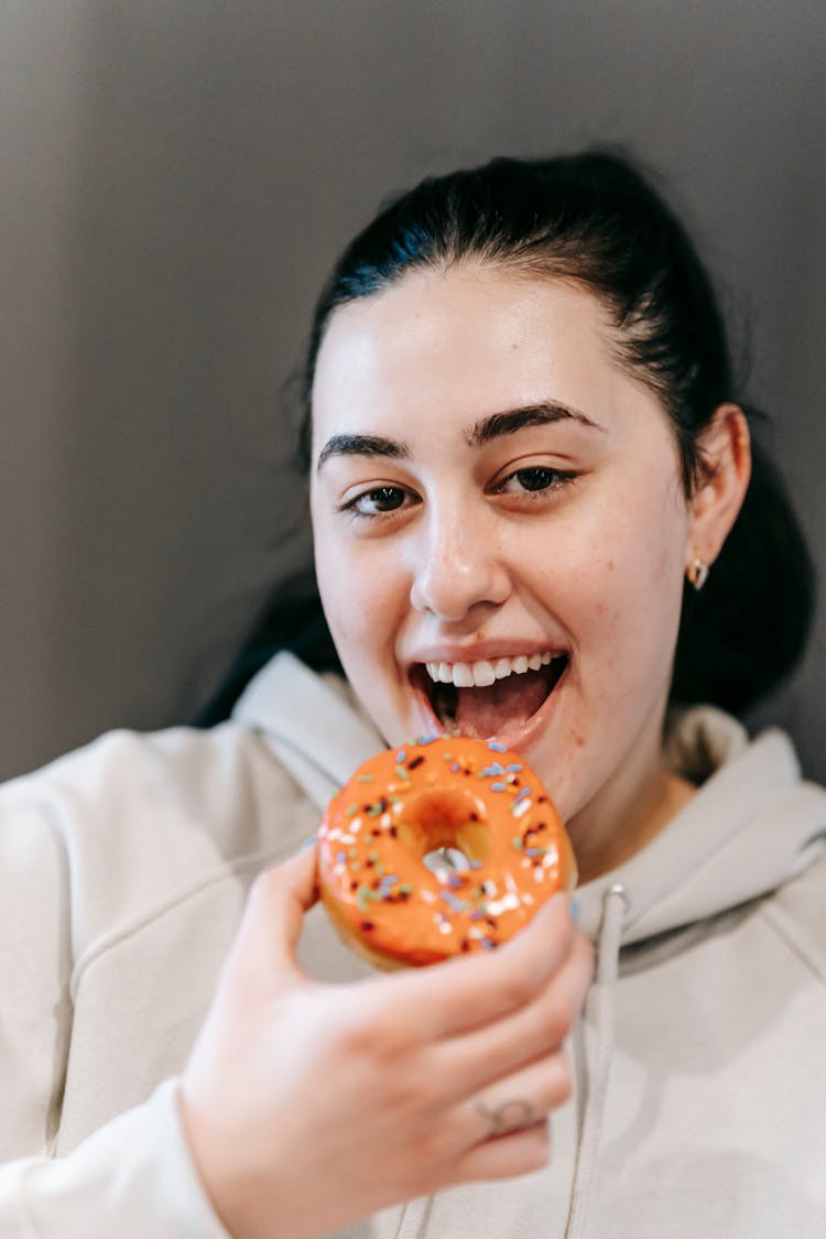 Cheerful Young Woman Biting Tasty Doughnut