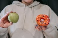Crop faceless woman demonstrating ripe green apple and sweet doughnut