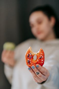 Close-up of a donut with sprinkles held by a woman, showcasing indulgence.