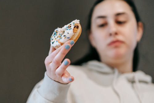 Free Crop emotionless female in casual wear chewing tasty doughnut glazed with vanilla icing in light room Stock Photo