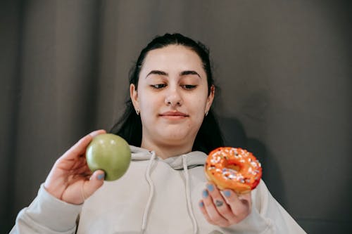 Free Positive woman choosing between donut and apple Stock Photo