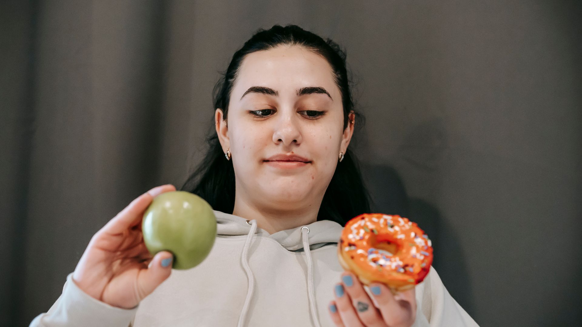 Modafinil vs Provigil: Unlocking the Truth Content young female in hoodie deciding between sweet unhealthy doughnut and green ripe apple in light room — modafinil vs provigil
