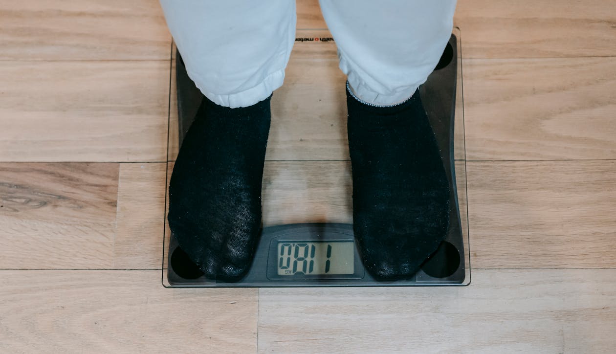 Free From above of crop unrecognizable plus size person in casual clothes standing on weighing scale on wooden floor Stock Photo