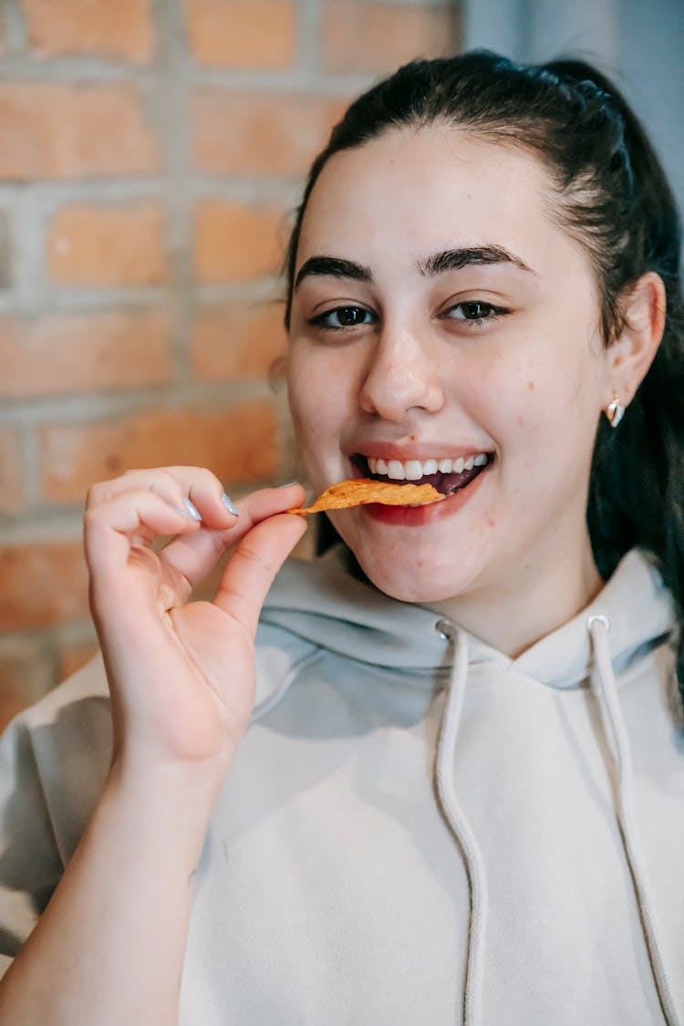 Excited Young Female Millennial Smiling And Eating Potato Crisps