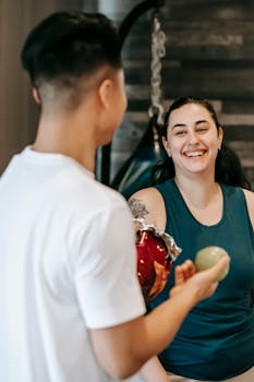 Anonymous young man offering apple and potato chips to cheerful obese female friend in gym