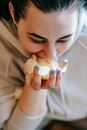 From above of crop female in sweater with black hair and handful of potato chips eating unhealthy fast food on blurred background