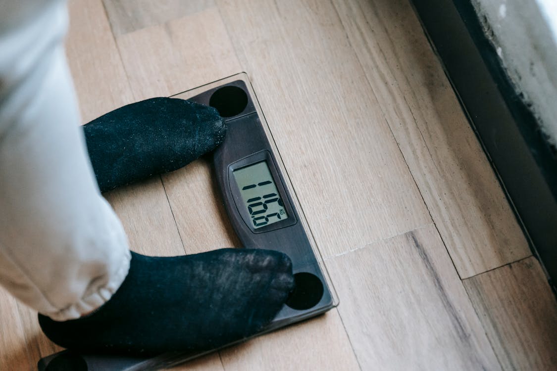 Free From above of unrecognizable person in socks standing on electronic weighing scales while checking weight on parquet during weight loss Stock Photo