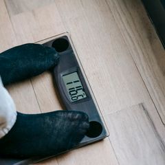 Feet in black socks on a black glass bathroom scale on a wooden floor