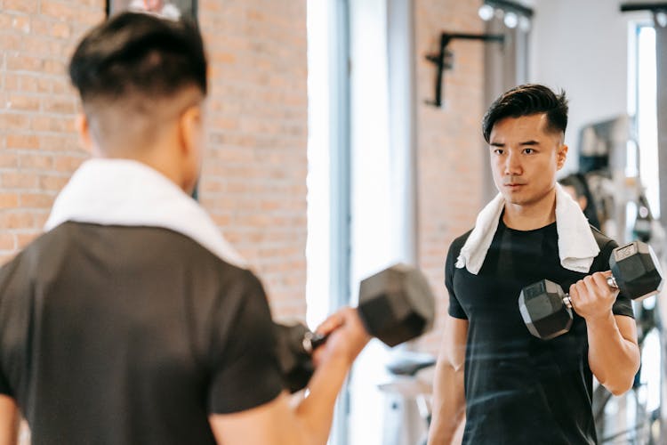 Determined Asian Man With Dumbbell In Gym