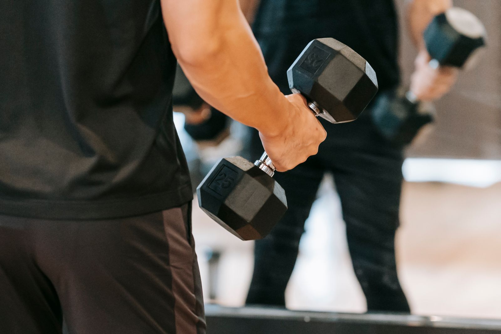 A man performing a dumbbell curl in front of a gym mirror