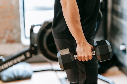 Side view of unrecognizable muscular male in black activewear lifting heavy weight while training in spacious fitness studio on blurred background