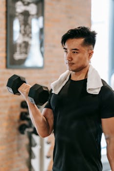 Determined Asian man lifting a dumbbell during workout in a modern gym.