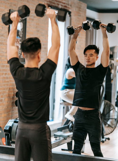 Strong Asian man raising dumbbells above head in gym